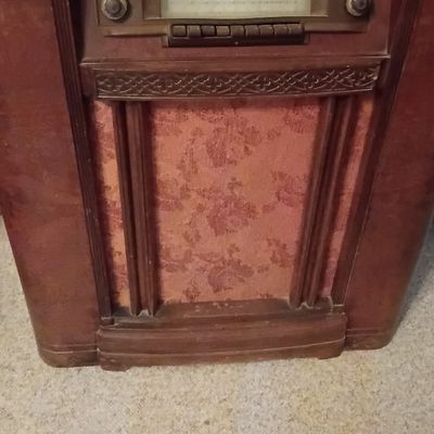 Vintage Art Deco wooden floor console radio with floral fabric speaker grille, showing some surface wear and age.