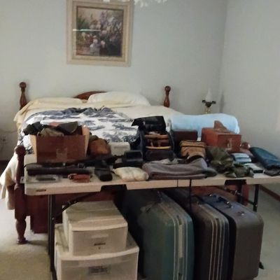 Bedroom featuring a wooden poster bed, a plastic folding table displayed with small items, and vintage hard-shell suitcases stored...