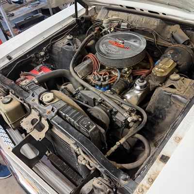 Engine bay of a classic Ford vehicle featuring a Ford Motorsport high-performance air cleaner and chrome valve covers, showing light...