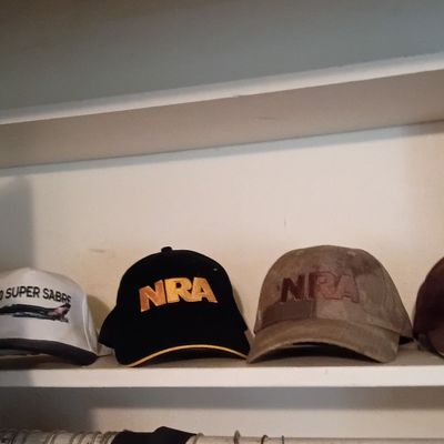 Collection of baseball caps displayed on a closet shelf, including NRA, Motorcraft, and F-100 Super Sabre designs.