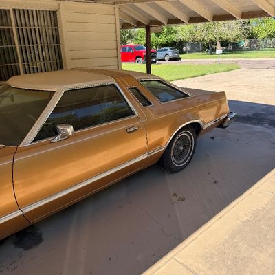 Vintage 1970s Ford Thunderbird coupe in gold finish, parked in a covered carport.