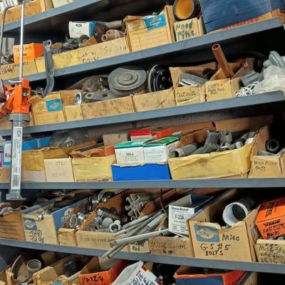 Metal workshop shelving unit packed with labeled cardboard bin boxes holding various auto parts and hardware.