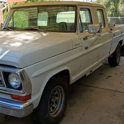 Vintage white Ford crew cab pickup truck parked under a covered carport, featuring original body styling and chrome front bumper.