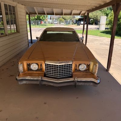 Vintage 1970s gold Ford Thunderbird coupe parked under a carport.