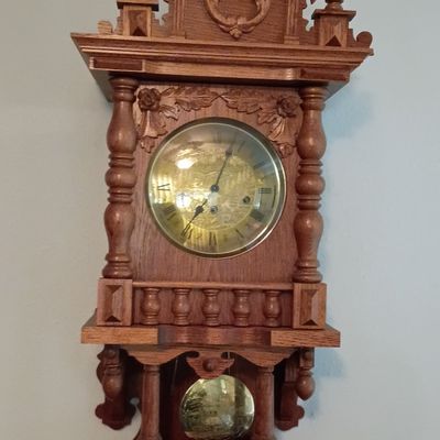 Vintage Zaandam-style wooden wall clock featuring ornate turned finials, detailed carvings, and a brass dial and pendulum.