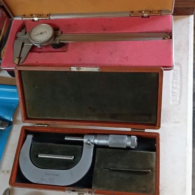 Vintage precision measuring tools, including dial calipers and an outside micrometer, housed in their protective fitted cases.