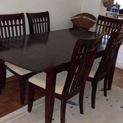 Dark wood dining set including a rectangular dining table and six matching chairs with vertical slat backs and upholstered seats.