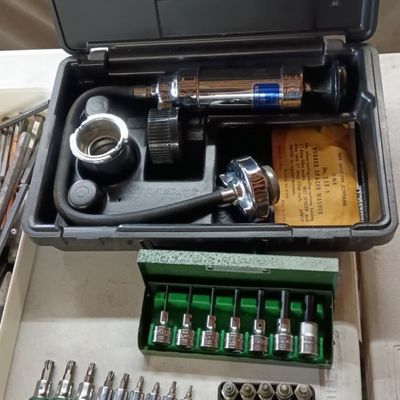 Vintage Stant cooling system pressure tester set in hard case, accompanied by various socket bit sets.
