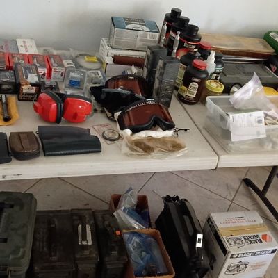 Assorted shooting supplies, ammunition reloading equipment, gun magazines, safety earmuffs, and metal ammo cans set on fold-out tables.