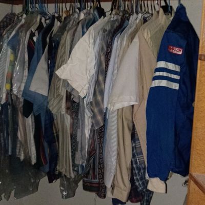 Closet full of men's vintage shirts, jackets, and bedding stored on top shelf.