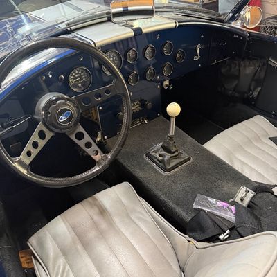 Interior view of a Shelby Cobra replica roadster featuring grey leather bucket seats, a Ford three-spoke steering wheel, and a blue...