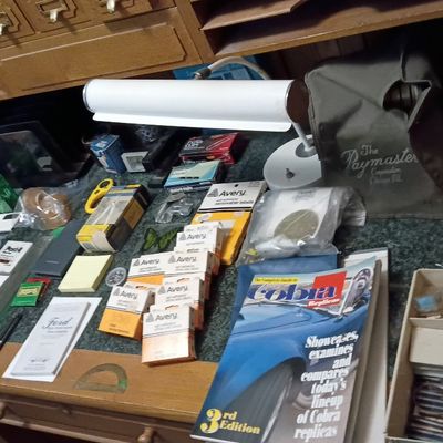 Wooden roll-top desk surface filled with various vintage and modern office supplies, including Avery labels, a Cobra Replicas magazine,...