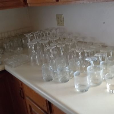 Large collection of vintage clear glassware, including stemware, tumblers, and serving dishes, displayed on a kitchen counter.