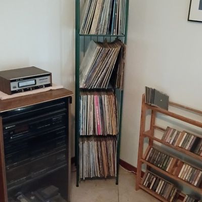 Vintage stereo component system in a glass-front wooden cabinet paired with a green metal arched shelf full of vinyl LP records.