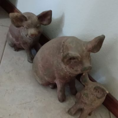 Set of three rustic stone or resin pig statues, including a larger pig with a piglet and a seated pig, featuring a distressed weathered...