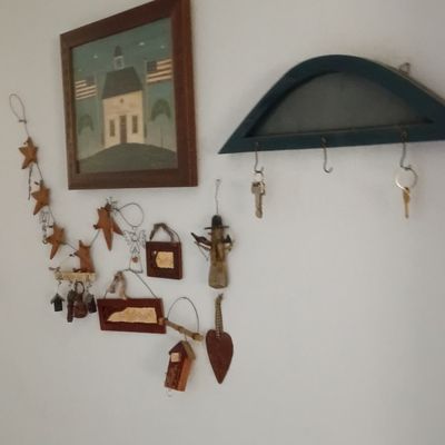 Rustic wall decor arrangement including a framed Americana schoolhouse painting, a blue arched key rack with hooks, and various small...