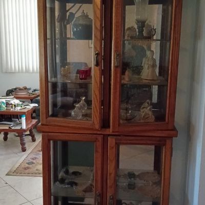 Two-tier wooden display cabinet featuring glass-front doors and interior shelving, holding various collectibles and decorative items.