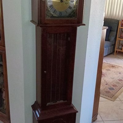Traditional dark wood grandmother clock featuring a broken arch pediment, finial, and brass dial with Roman numerals.