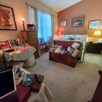Sale Photo Thumbnail #105: Bedroom featuring a metal bed frame, wooden chests, framed artwork, and display tables filled with collectibles and accessories.