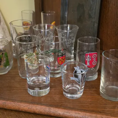 Sale Photo Thumbnail #75: Collection of souvenir glasses and shot glasses featuring various graphics and logos, including Hard Rock Cafe and German festival designs.