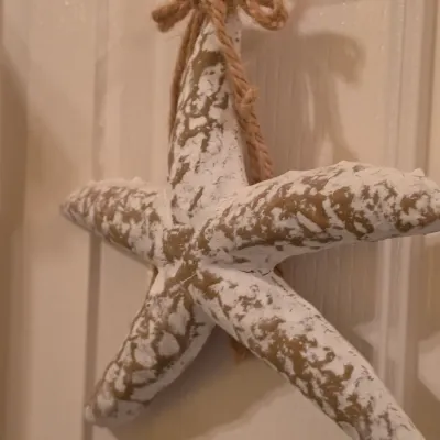 Sale Photo Thumbnail #259: Coastal-style distressed white and gold painted starfish hanging wall accent featuring a rustic twine bow.