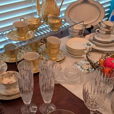 Sale Photo Thumbnail #102: Collection of fine china tea sets, crystal stemware, and serving pieces displayed on a table.