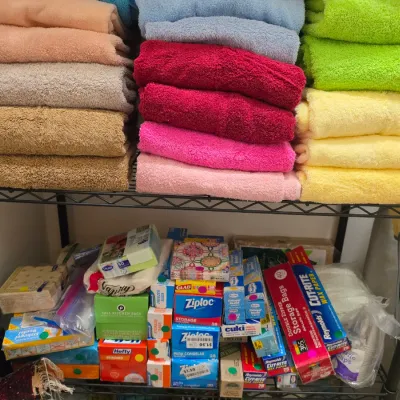 Sale Photo Thumbnail #269: Wire shelving unit filled with neatly folded bath towels in various bright colors on the top shelf, and an assortment of household paper goods, food storage bags, and wrap on the bottom shelf.