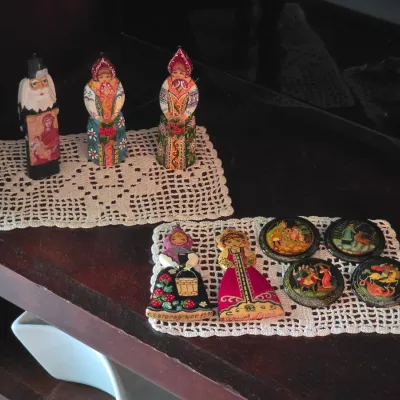 Sale Photo Thumbnail #89: Collection of hand-painted Russian folk art figurines and lacquer pin brooches arranged on small crocheted doilies.