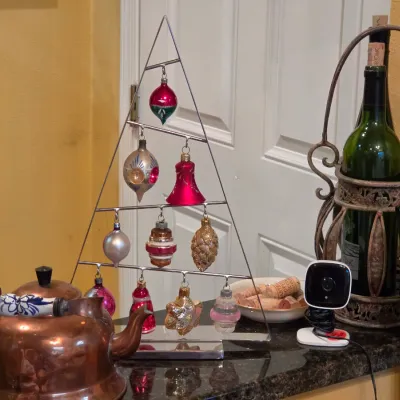 Sale Photo Thumbnail #53: A tabletop metal wire Christmas tree ornament display stand featuring various vintage glass ornaments, set alongside a copper kettle and a wrought iron wine bottle caddy.