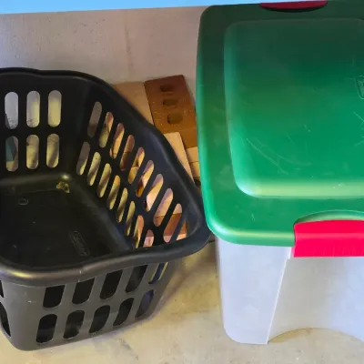 Sale Photo Thumbnail #280: Black plastic laundry basket sitting next to a Sterilite plastic storage tote with a green lid and red handles.