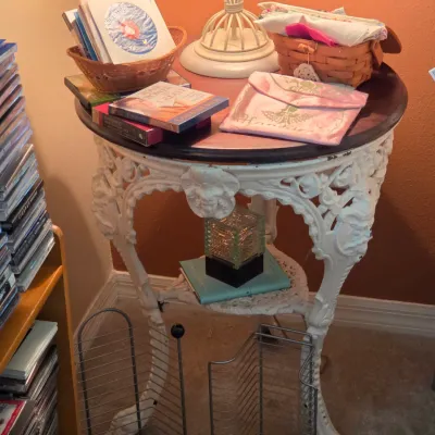 Sale Photo Thumbnail #111: Ornate white cast metal accent table with a dark wooden top, holding books, a basket, and small decorative items.