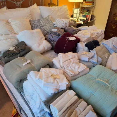 Sale Photo Thumbnail #121: Large collection of folded linens, blankets, and bedsheet sets with price tags arranged on a bed.