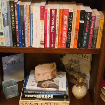 Sale Photo Thumbnail #219: Wooden bookcase filled with a varied collection of hardcover and paperback books, decorative pottery, and small art pieces.