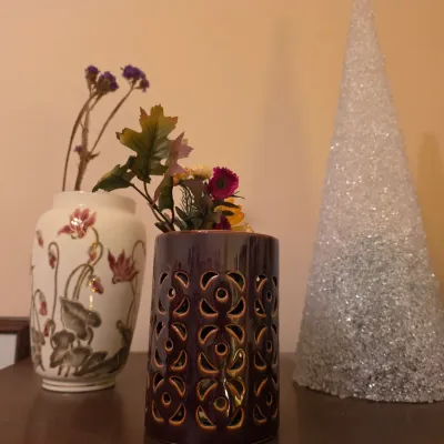 Sale Photo Thumbnail #252: Collection of decorative items featuring a pierced dark ceramic vase with faux florals, a porcelain floral vase, and a glittery cone tree sculpture.