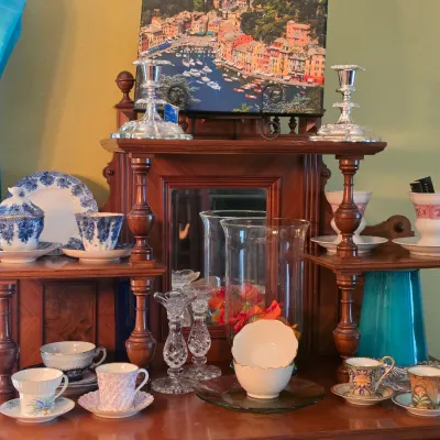 Sale Photo Thumbnail #100: Collection of assorted vintage porcelain teacups, glass candlesticks, and silver-plated candle holders displayed on a multi-tiered wooden shelf unit.