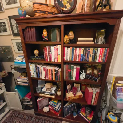 Sale Photo Thumbnail #224: Tall dark wood dual-column bookcase filled with a wide variety of hardcover and paperback books, decorative eggs, small figurines, and collectibles.