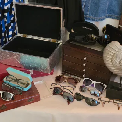 Sale Photo Thumbnail #132: Collection of women's sunglasses, prescription eyeglasses, and jewelry storage boxes, alongside a decorative seashell sculpture on a stand.
