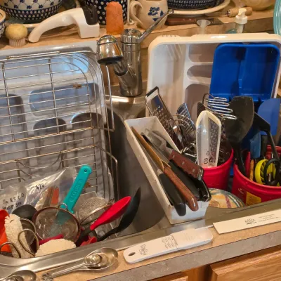 Sale Photo Thumbnail #14: Collection of assorted kitchen utensils, dish drying racks, mesh strainers, measuring spoons, and cutlery displayed inside a kitchen sink.
