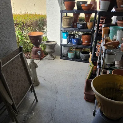 Sale Photo Thumbnail #343: Collection of outdoor garden supplies including ceramic planters, terracotta pots, urns, and metal folding patio chairs.