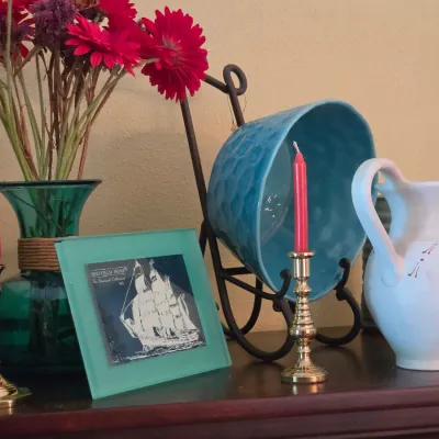 Sale Photo Thumbnail #91: Tabletop decorative ensemble featuring brass candlesticks with pink candles, a green glass vase with flowers, a Sheffield Home glass frame, and ceramic pitchers.
