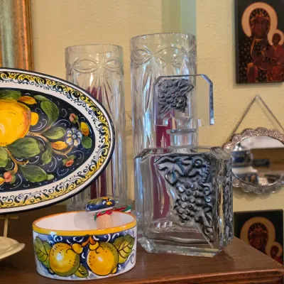 Sale Photo Thumbnail #73: Collection of decorative tabletop decor including an Italian majolica lemon-patterned platter and bowl, crystal vases, and a heavy cut crystal decanter featuring a grape motif.
