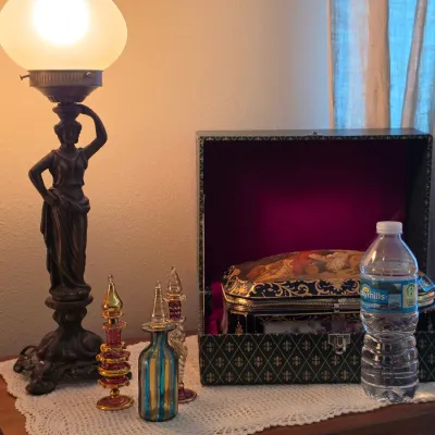 Sale Photo Thumbnail #125: Neoclassical style figural bronze table lamp with a frosted glass globe shade, shown beside ornate perfume bottles and an embellished jewelry box.