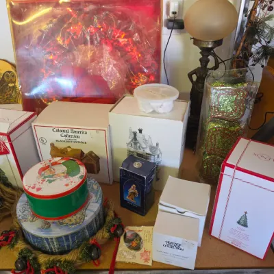 Sale Photo Thumbnail #290: Collection of holiday decor and collectibles including boxed Dept 56 Christmas village buildings, Lenox ornaments, festive tins, and a table lamp.