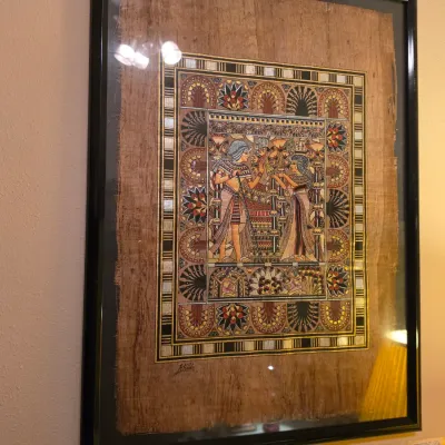 Sale Photo Thumbnail #250: Framed hand-painted Egyptian papyrus art featuring traditional figures and elaborate floral borders in a black composite frame.