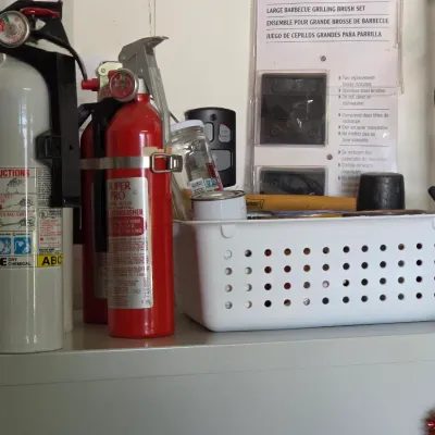 Sale Photo Thumbnail #285: Pair of Kidde fire extinguishers, including one white and one red model, sitting alongside a white plastic perforated storage basket on a shelf.