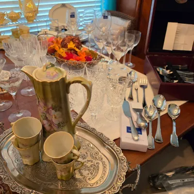 Sale Photo Thumbnail #103: A dining table displayed with crystal glassware, a hand-painted floral chocolate pot set on an etched silver tray, flatware, and a wooden silverware chest.