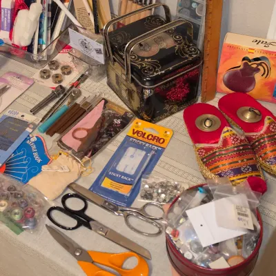Sale Photo Thumbnail #168: Collection of sewing supplies, including bobbins, scissors, vintage Singer tin, Velcro, needles, alongside a boxed pair of Jale Spanish castanets and decorative slippers.