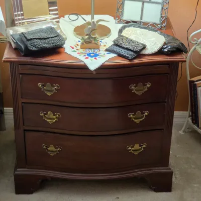 Sale Photo Thumbnail #108: Traditional mahogany three-drawer nightstand with brass swan-neck pulls, displaying vintage beaded purses and decor items on top.