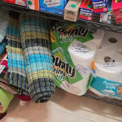 Sale Photo Thumbnail #270: Assortment of household goods on a wire shelf, including rolled woven accent rugs, Bounty paper towels, and Angel Soft toilet paper.