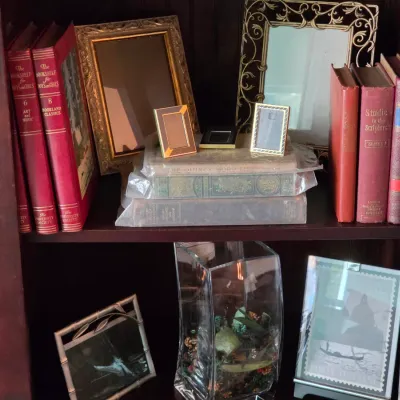 Sale Photo Thumbnail #87: Collection of vintage picture frames, antique hardbound books, and decorative home accessories displayed on wooden bookcase shelves.